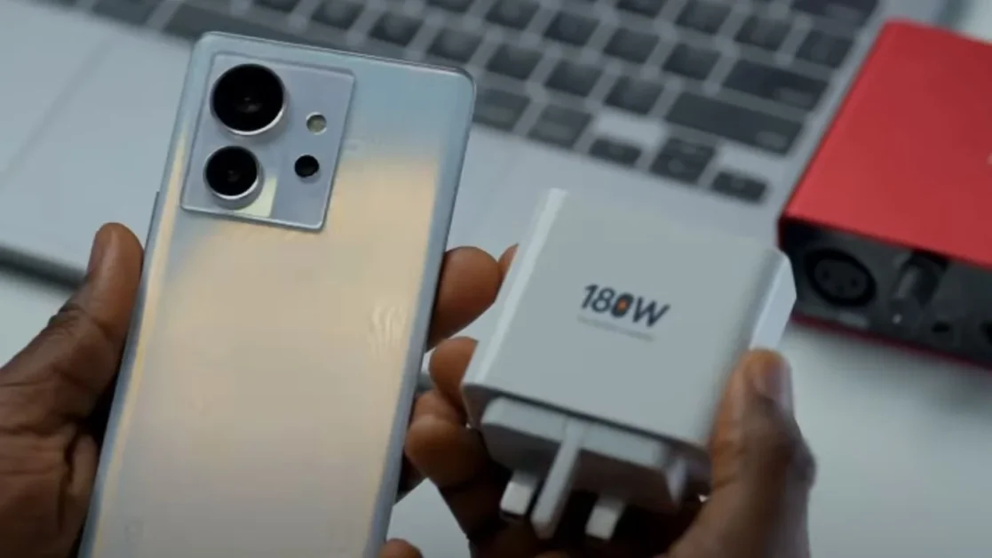 Hand holding Infinix Zero Ultra smartphone and 180W fast charger.